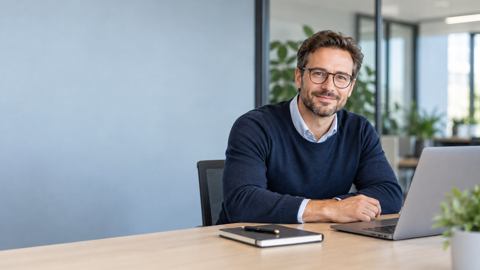Freundlich lächelnder IT-Berater an einem Schreibtisch mit Laptop in einem hellen Büro